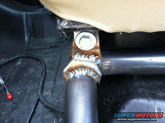 Welded seat bracket on metal tubing, with tan upholstery and black flooring visible