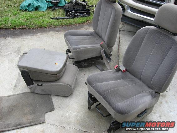 Two gray cloth vehicle seats and a gray center console with storage compartment, on concrete