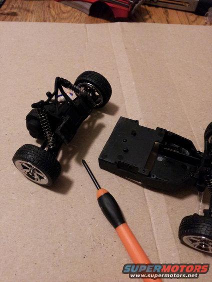 Remote control car chassis and suspension components with a screwdriver. Supermotors.net logo visible