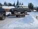 1979 Ford Bronco - A dark gray Ford Bronco is loaded onto a trailer, being towed by a black truck through a snowy landscape.