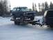 1979 Ford Bronco - A dark gray 1978 Ford Bronco, partially covered in snow, is transported on a trailer towed by a black SUV through a wintery scene.