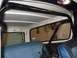 1979 Ford Bronco - The interior of a vehicle shows a roll cage and blue upholstered seats, with a view through the rear window.