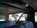 1979 Ford Bronco - The interior of a 1978 Ford Bronco, showing the rear bench seat and a roll cage, with a view of houses and trees through the windows.