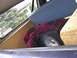 1979 Ford Bronco - A subwoofer and blanket are stored in the cargo area of a vehicle, with a view of trees and a house through the window.