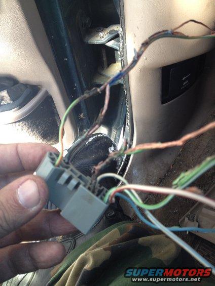 Hand holding gray wiring harness connector with frayed wires