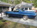 1972 Ford Ranchero - A blue 1972 Ford Ranchero is parked in a driveway, with a white pickup truck visible behind it under a large tarp.