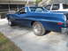 1972 Ford Ranchero - A blue 1972 Ford Ranchero is parked in front of a garage, with a white pickup truck behind it.