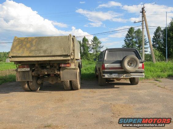 1987 Ford Bronco with spare tire mounted on rear door, dark grey and red body, parked on dirt road