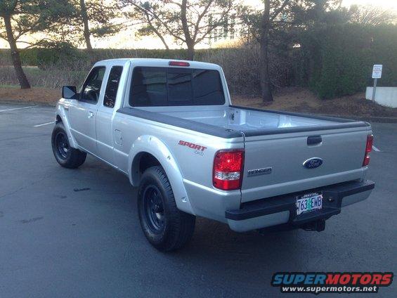 Silver Ford Ranger pickup truck parked on asphalt, trees in background. Has a 'Sport 4x4' decal on the fender