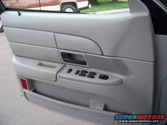 Car door panel with window controls and speaker grille. Another vehicle is visible outside