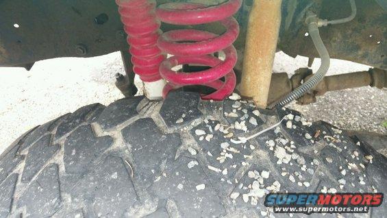 Tire covered in gravel with red coil spring and shock absorber visible