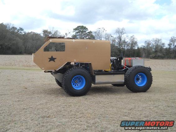 Tan custom off-road vehicle with blue wheels and a black star emblem on the side, viewed from the left