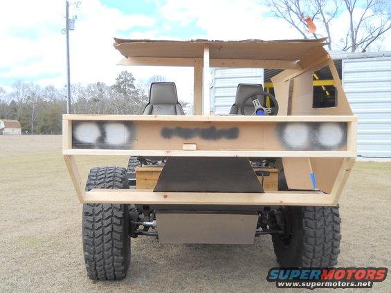 Rear view of a homemade vehicle replica constructed from cardboard and wood, showing seats and a steering wheel inside