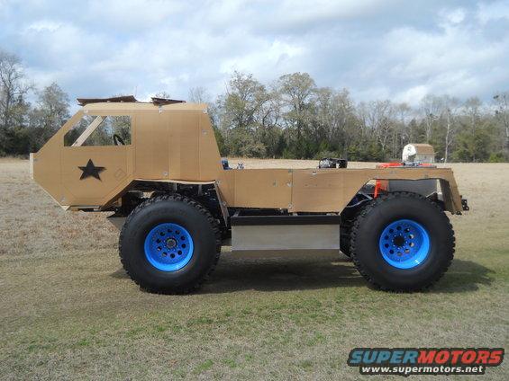Custom off-road vehicle with large tires and blue rims, made of tan material with a black star on the side