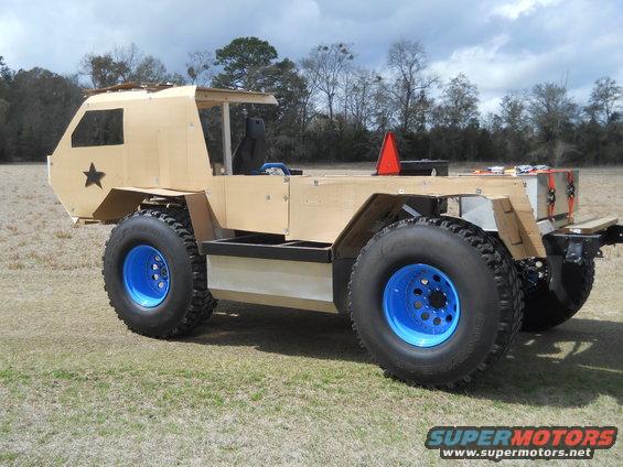 Custom off-road vehicle with large tires and blue rims, unfinished wooden body, black star emblem