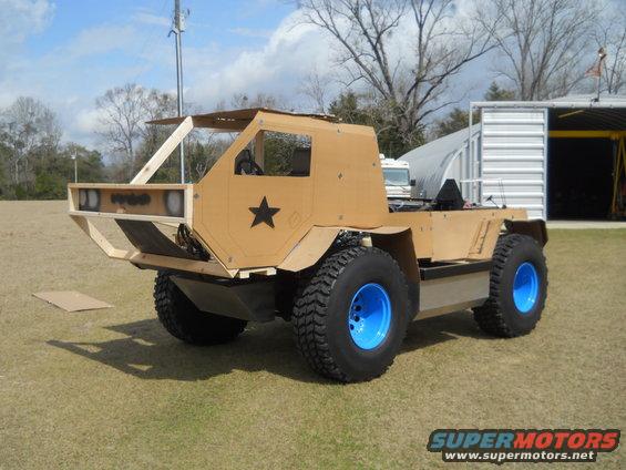 Cardboard-bodied custom vehicle with large tires and blue rims, seen from a 3/4 front angle