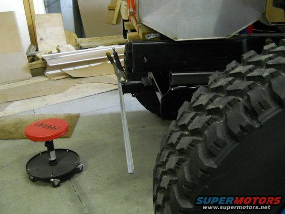 Close-up of a large off-road tire and part of a vehicle's frame, with a red mechanic's stool nearby