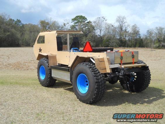 Custom-built off-road vehicle with large tires and a tan body, parked in a grassy field