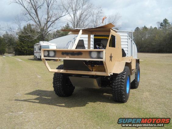 custom off-road vehicle with large tires, blue rims, and a wooden frame, parked on grass