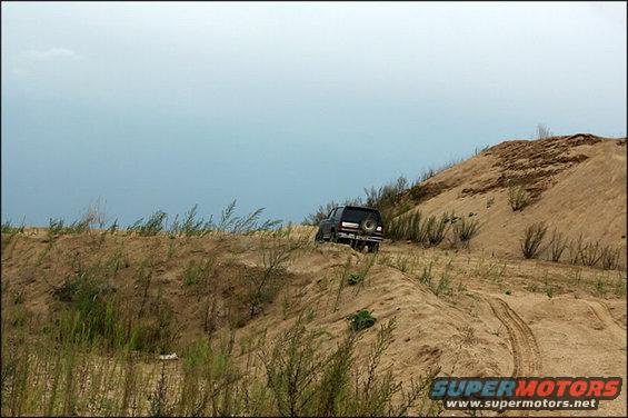 1987 Ford Bronco driving up a sand dune, rear view. Spare tire mounted on the back