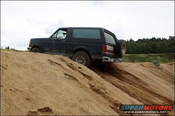 Black 1987 Ford Bronco driving up a sand dune, rear-mounted spare tire visible