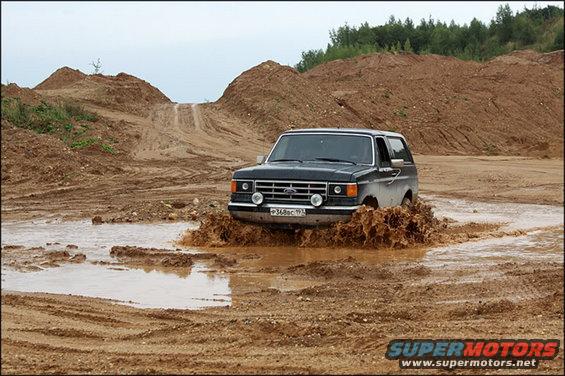 Black 1987 Ford Bronco driving through mud, front view