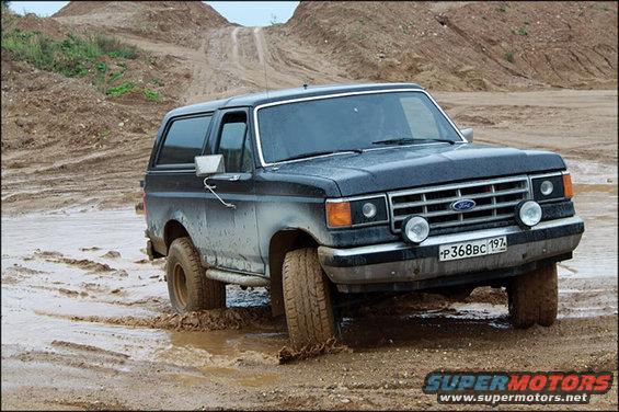 Black 1987 Ford Bronco driving through mud