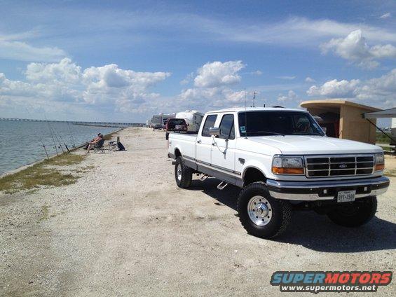 1997 Ford F-350 pickup truck parked by the water with fishing rods and campers in the background. License plate reads BYT-7509