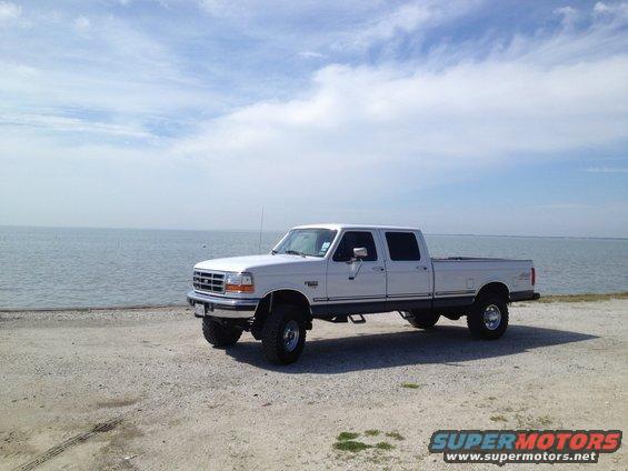 White 1997 Ford F-350 crew cab pickup truck parked on a gravel lot near the water