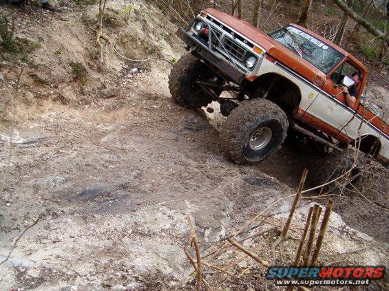 Orange and white pickup truck with large tires climbing a muddy hill