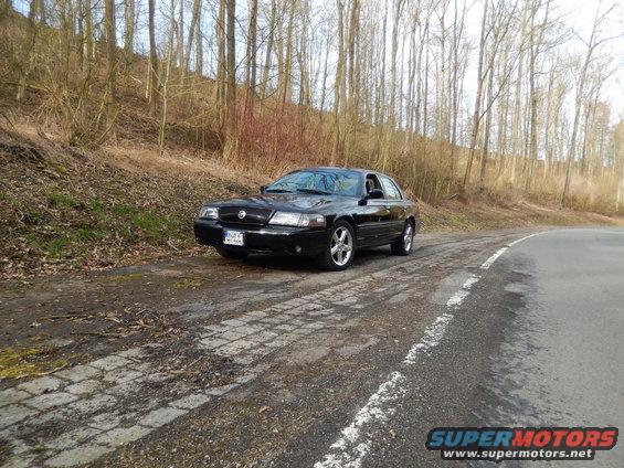 Black 2003 Mercury Marauder parked on a dirt road next to a wooded hill