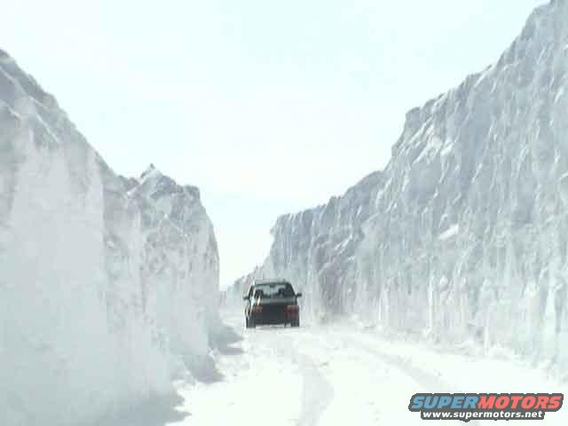 Car driving on a snow-covered road between tall snow walls