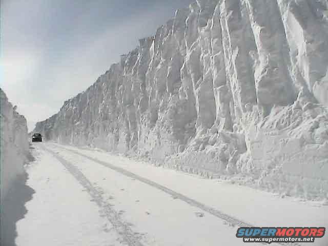 Car driving on a snow-covered road with high snow walls on the side