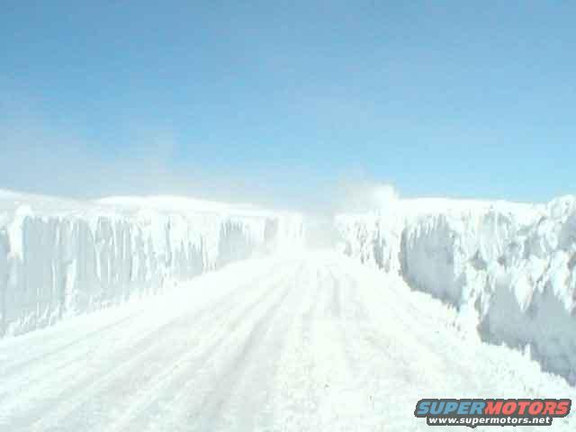 Snow-covered road with high snow walls under a blue sky