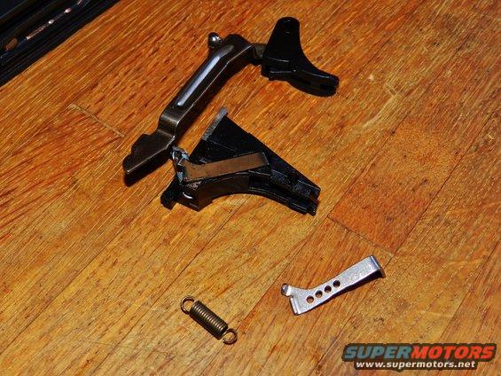 Gun trigger assembly parts and spring on wooden floor. Includes metal and black plastic components