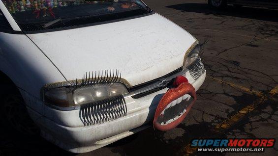 White car with fake eyelashes on headlights and a large set of lips with fangs on the bumper