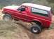 1996 Ford Bronco - A man drives a red Ford Bronco through a challenging off-road terrain, with one tire lifted high.