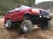 1996 Ford Bronco - A red 1996 Ford Bronco is shown off-roading on a dirt path with hills in the background.