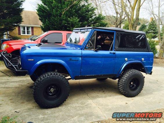 Blue 1974 Ford Bronco with black soft top and off-road tires parked on concrete