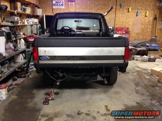 1992 Ford Bronco rear view, showing tailgate and interior through open doors. Vehicle is in a garage with tools and shelves