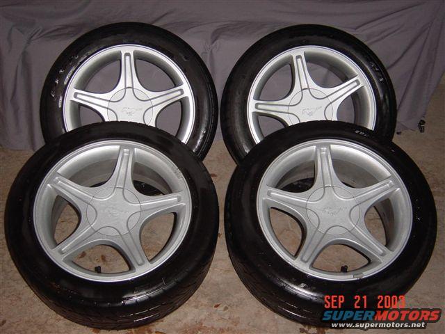 four silver 5-spoke wheels with black tires, each center cap has a horse emblem