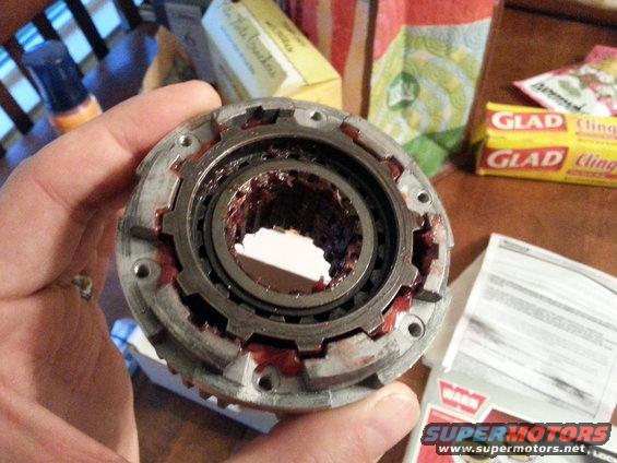 Close-up of a Warn locking hub part, greased and held by a hand. A "WARN" logo is visible on a document in the background