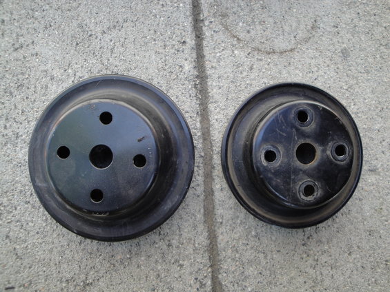 Two black automotive pulleys with circular mounting holes, resting on a concrete surface
