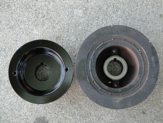 Two crankshaft pulleys, one black and one rusty, on concrete