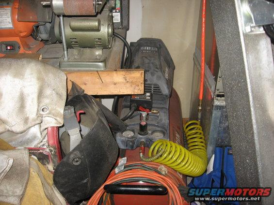 Red air compressor with black top, yellow coiled hose, and orange power cord