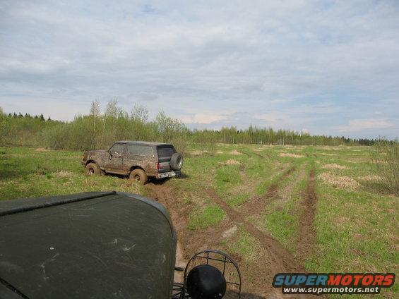 1987 Ford Bronco stuck in mud on a grassy field with tire tracks