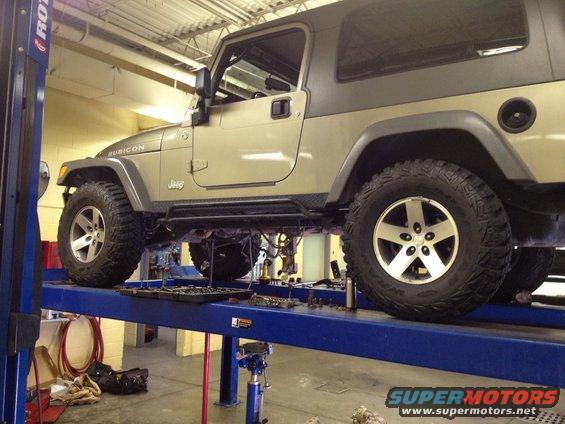 Jeep Wrangler on a lift, showing the side profile and undercarriage. It has 'Rubicon' and 'Jeep' badges
