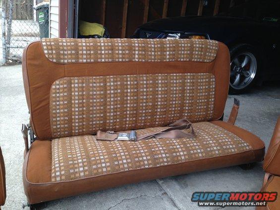 Brown and tan plaid car seat with seatbelt in garage, another car visible behind