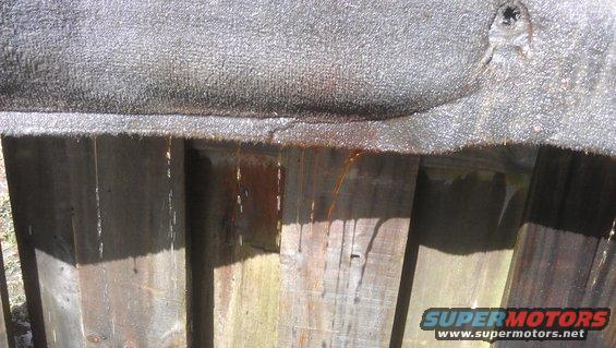 Water drips from a textured surface onto a wooden fence
