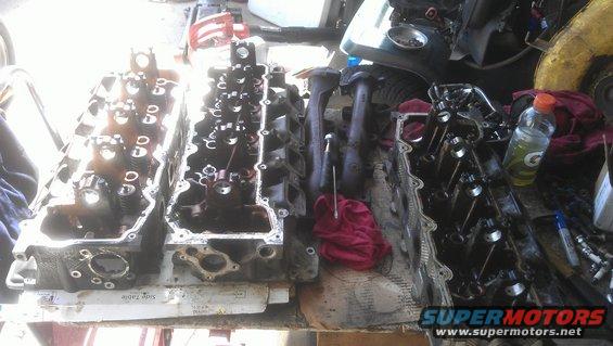 Engine cylinder heads and exhaust manifolds on a table, with a bottle of Gatorade and tools nearby